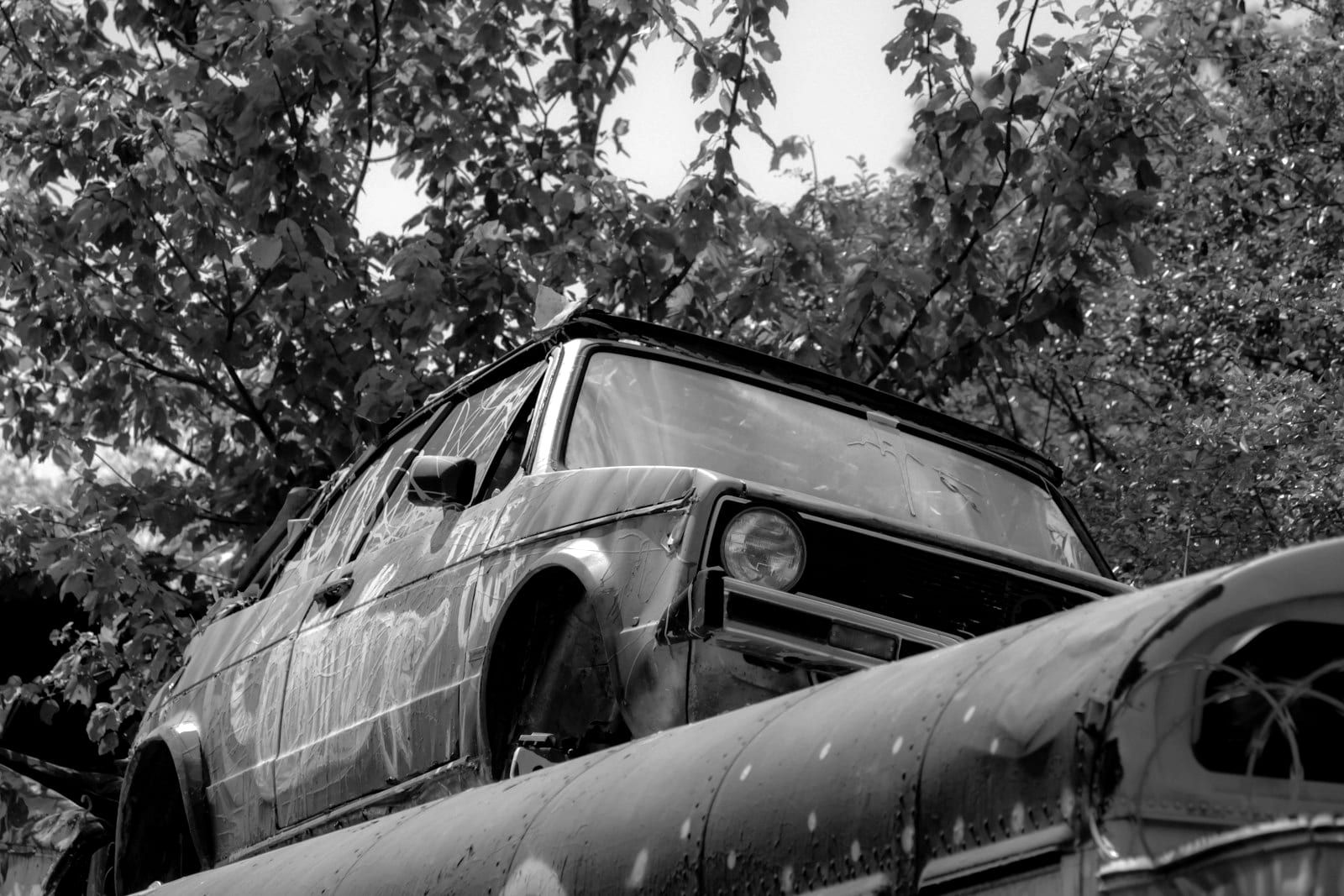 A rusted, stripped car body sitting on top of a trailer among trees